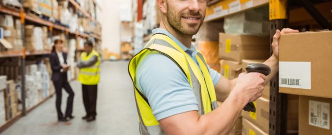 Warehouse worker scanning box while smiling at camera in a large warehouse